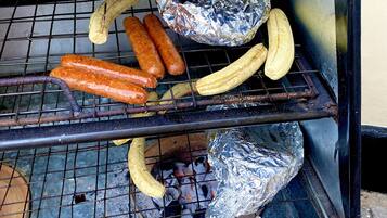 Un barbecue avec des saucisses, des bananes et des aliments enveloppés dans du papier d’aluminium qui cuisent.