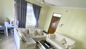 Una sala de estar con un sofá modular, una mesa de centro, un televisor y un comedor con una mesa y sillas.