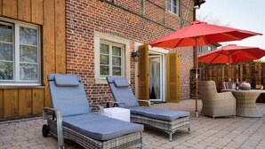 Une terrasse avec deux chaises longues et une table, un parasol rouge et des meubles en osier.