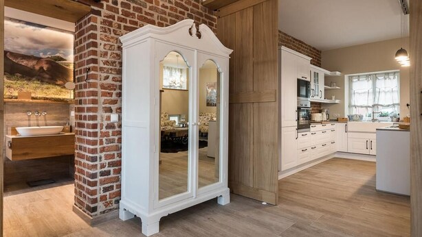 Une cuisine moderne avec des meubles blancs, un mur d’accent en briques et un grand meuble blanc doté de portes en verre.
