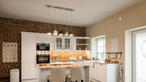 Une cuisine moderne avec des armoires blanches, un mur d’accent en briques et un îlot central doté de tabourets de bar.
