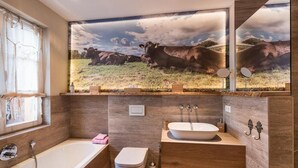 Une salle de bain équipée d’une baignoire, de toilettes et d’un lavabo, avec une fresque représentant une vache peinte sur le mur.