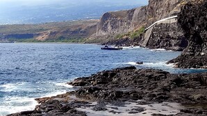 A coastal landscape with rocky terrain and a road curving along the cliffside. - Chambre Privée Chez Jo, en Bordure de Savane (Saint Paul)