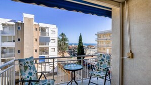 Ein Balkon mit zwei Stühlen und einem kleinen Tisch, der auf eine Straße mit Gebäuden und Palmen blickt.