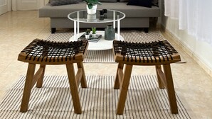 Ein modernes Wohnzimmer mit einem grauen Sofa, einem Glastisch, zwei Holzstühlen, einer kleinen Pflanze und zwei abstrakten Wandbildern.