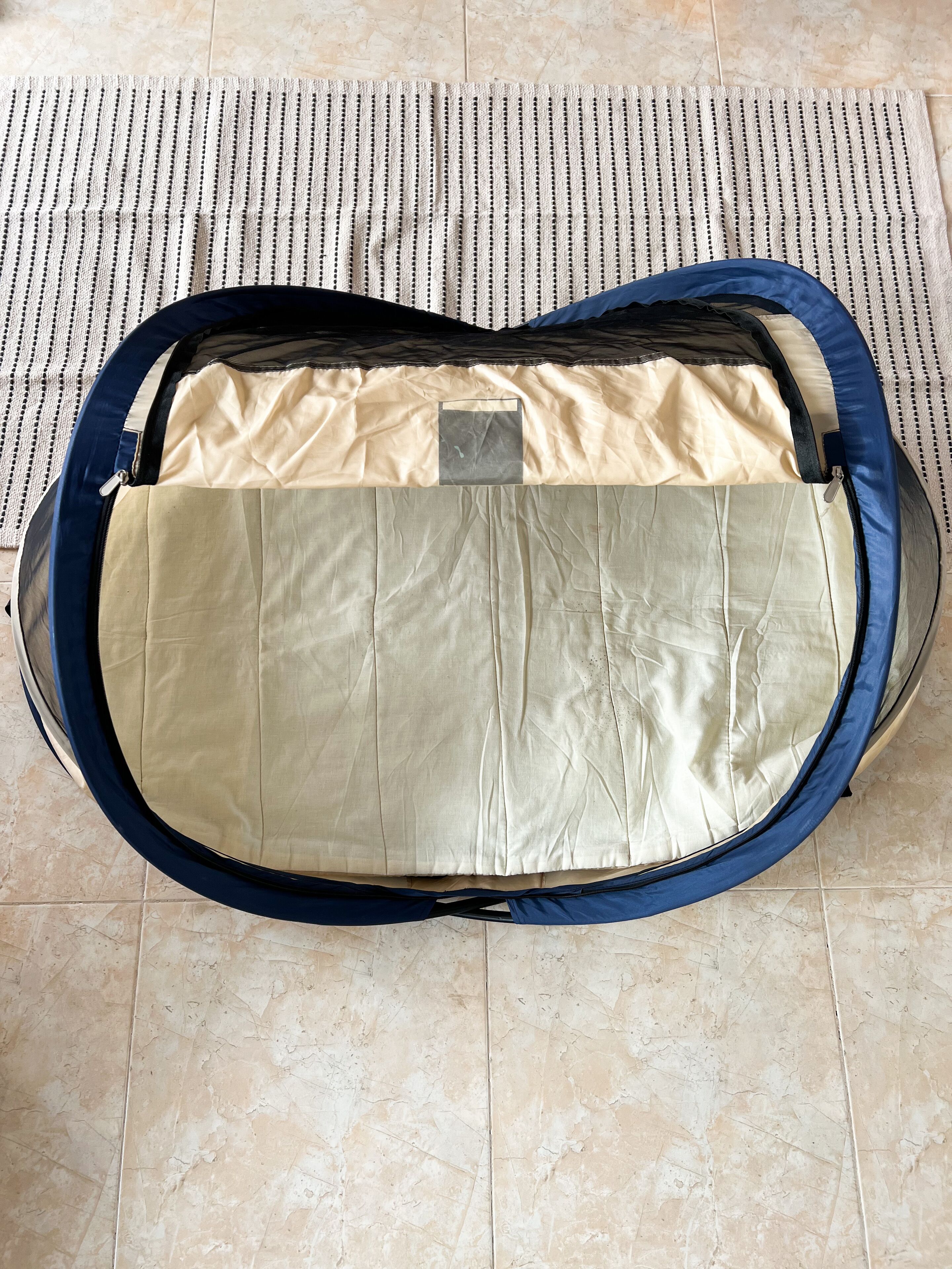 Un'ampia valigia vuota, beige all'interno e blu all'esterno, posata su un pavimento piastrellato.