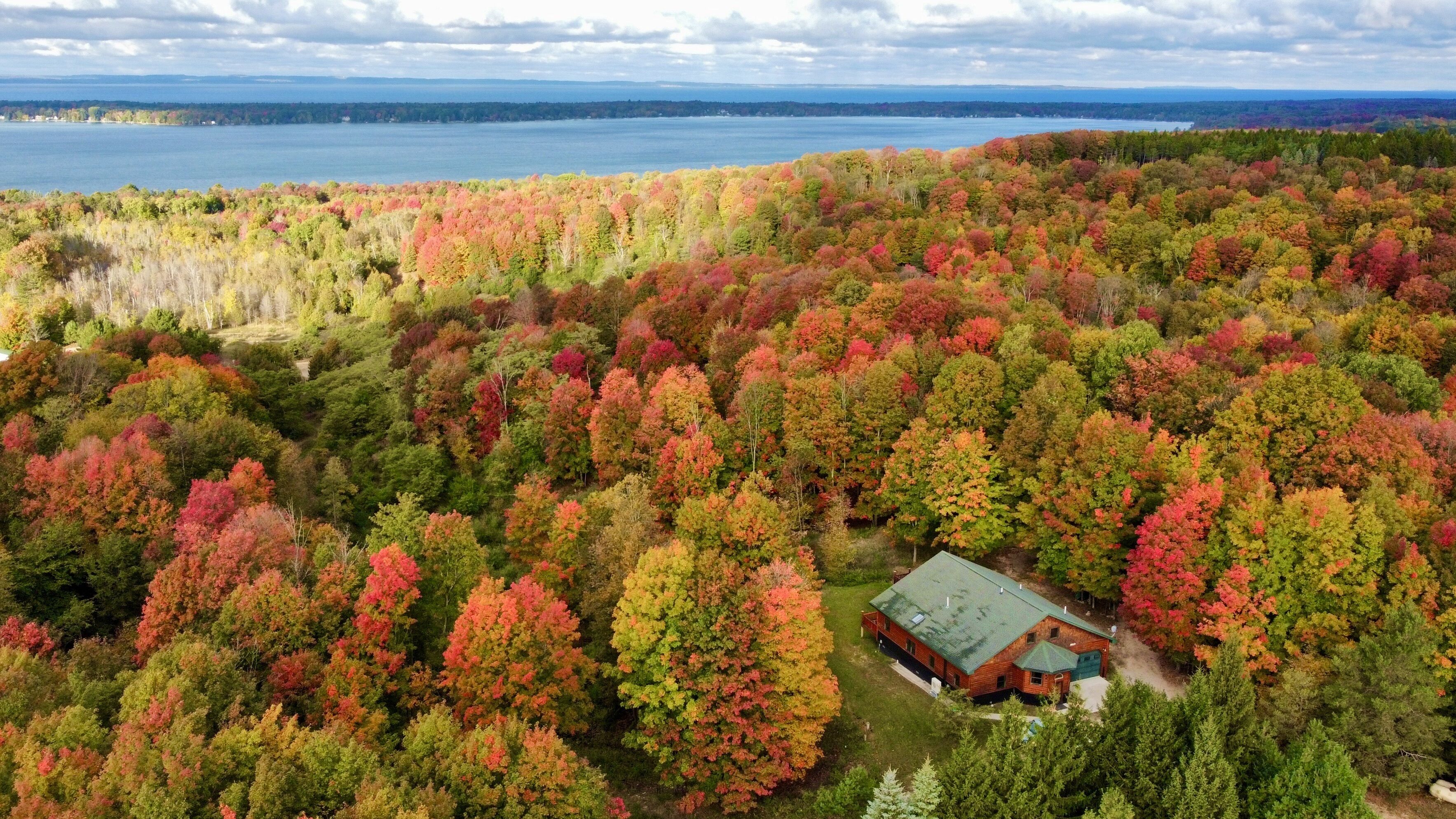 Vue aérienne d’une zone boisée avec une cabane entourée d’arbres aux couleurs automnales.