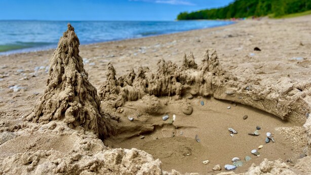 A sandy beach with a large sandcastle and scattered pebbles.