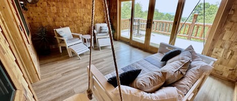 A wooden cabin with a bed, chairs, and a balcony with a view.