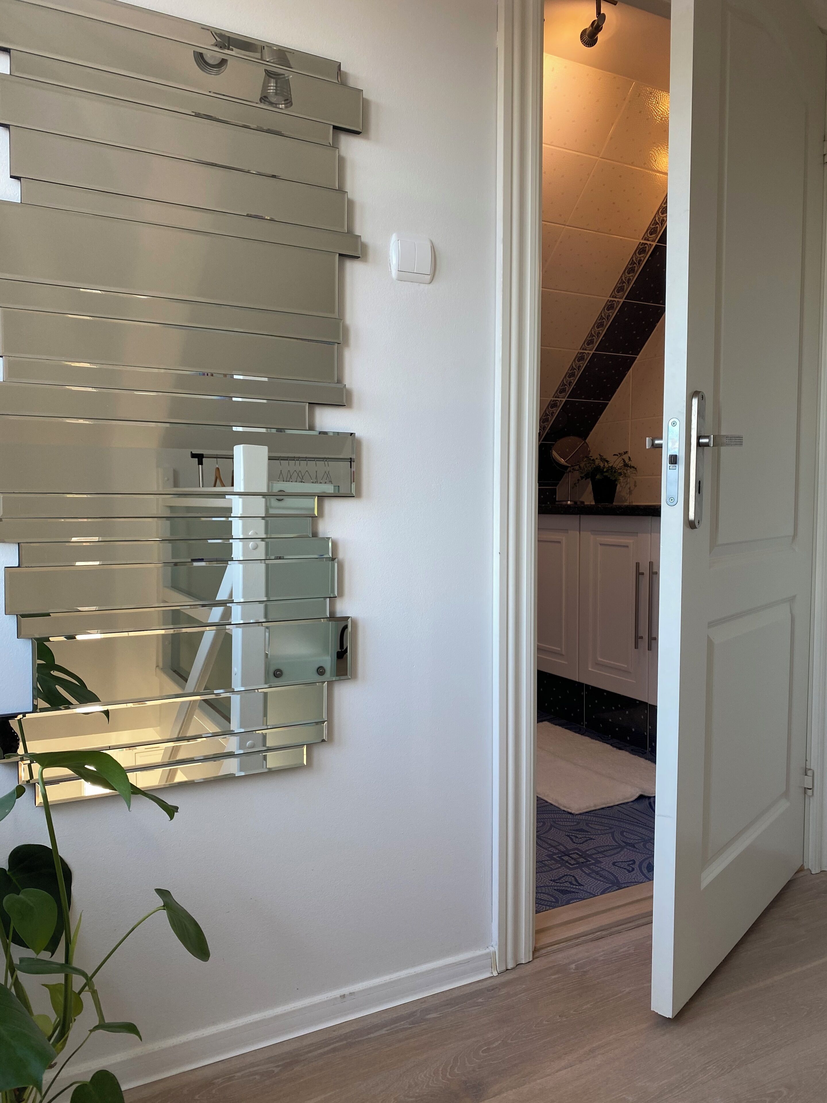 Un pasillo con un mueble de almacenaje moderno con puerta de vidrio, una puerta blanca y una escalera que conduce a otra habitación.