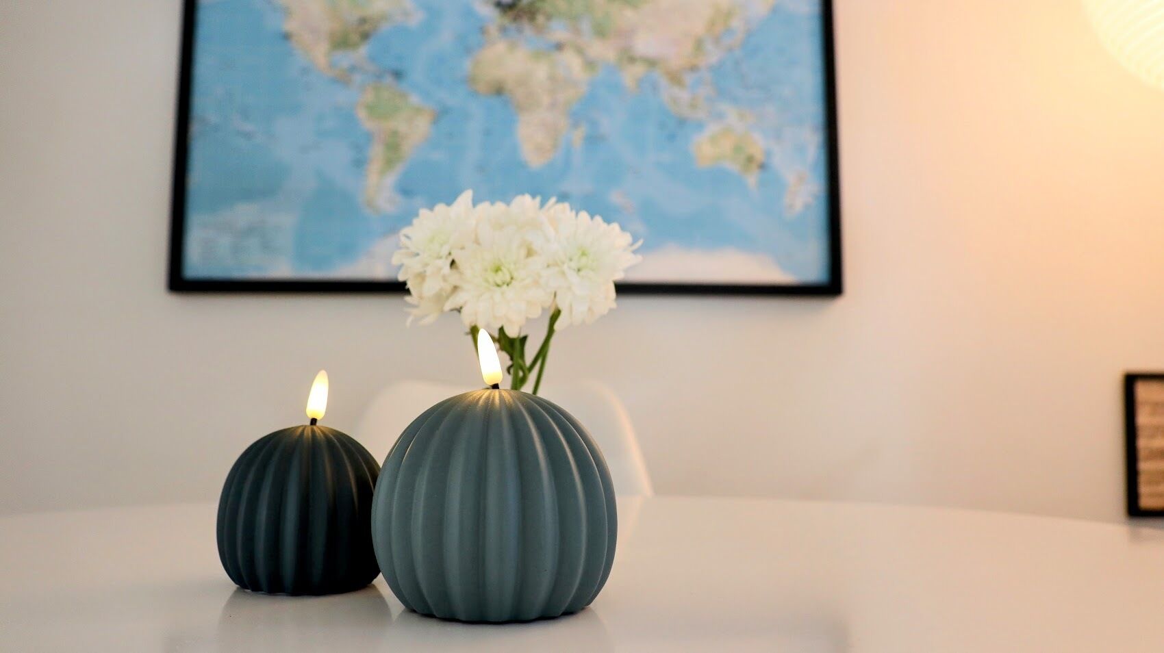 Dos jarrones esféricos con velas sobre una mesa blanca, una silla blanca y un mapa del mundo en la pared.