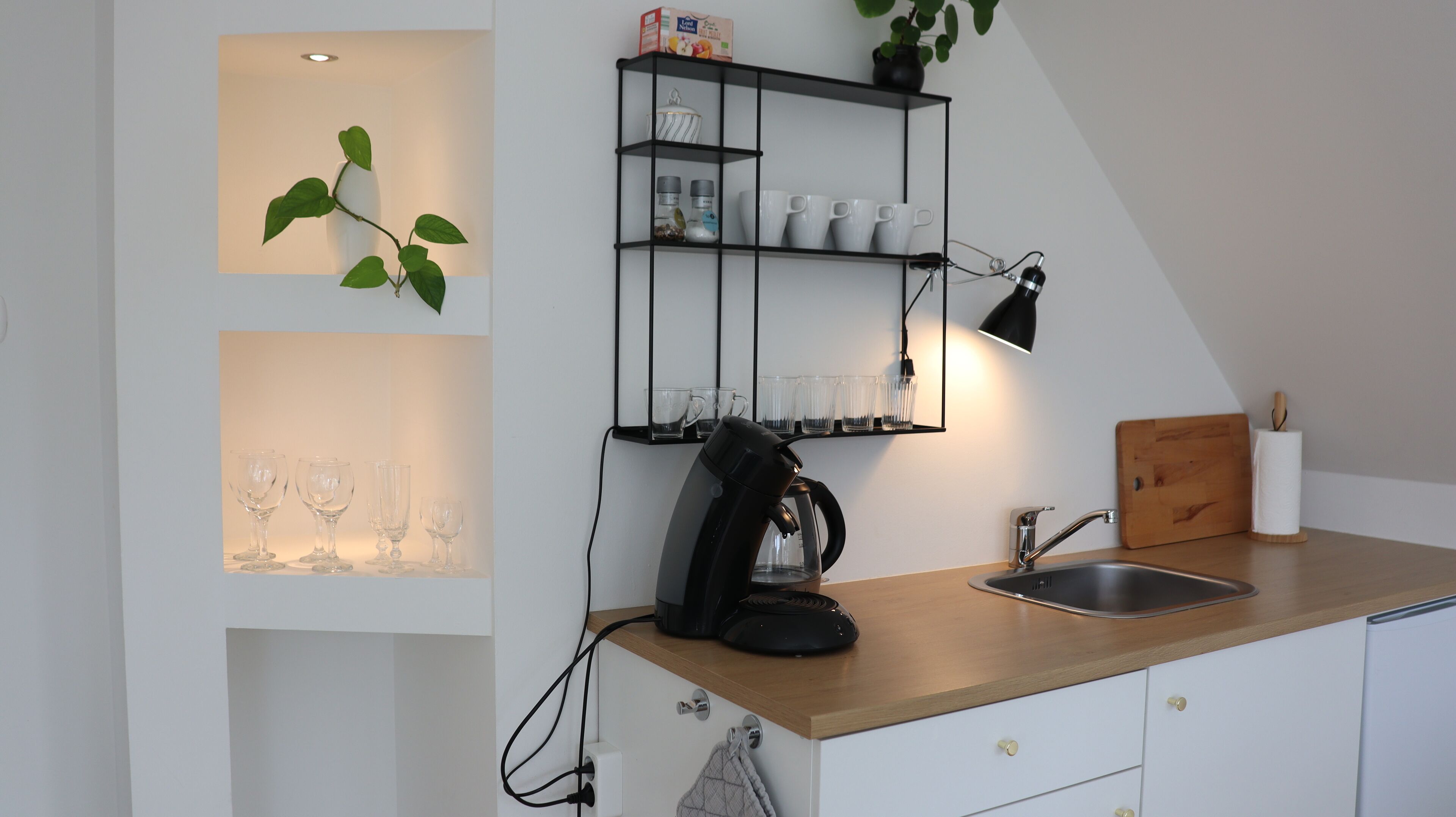 Et moderne køkken med kaffemaskine, en hylde med kopper og en plante.