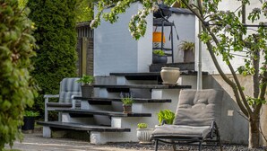 A garden with a chair, a potted plant, and a white wall. - Møllehuset (Ikast)