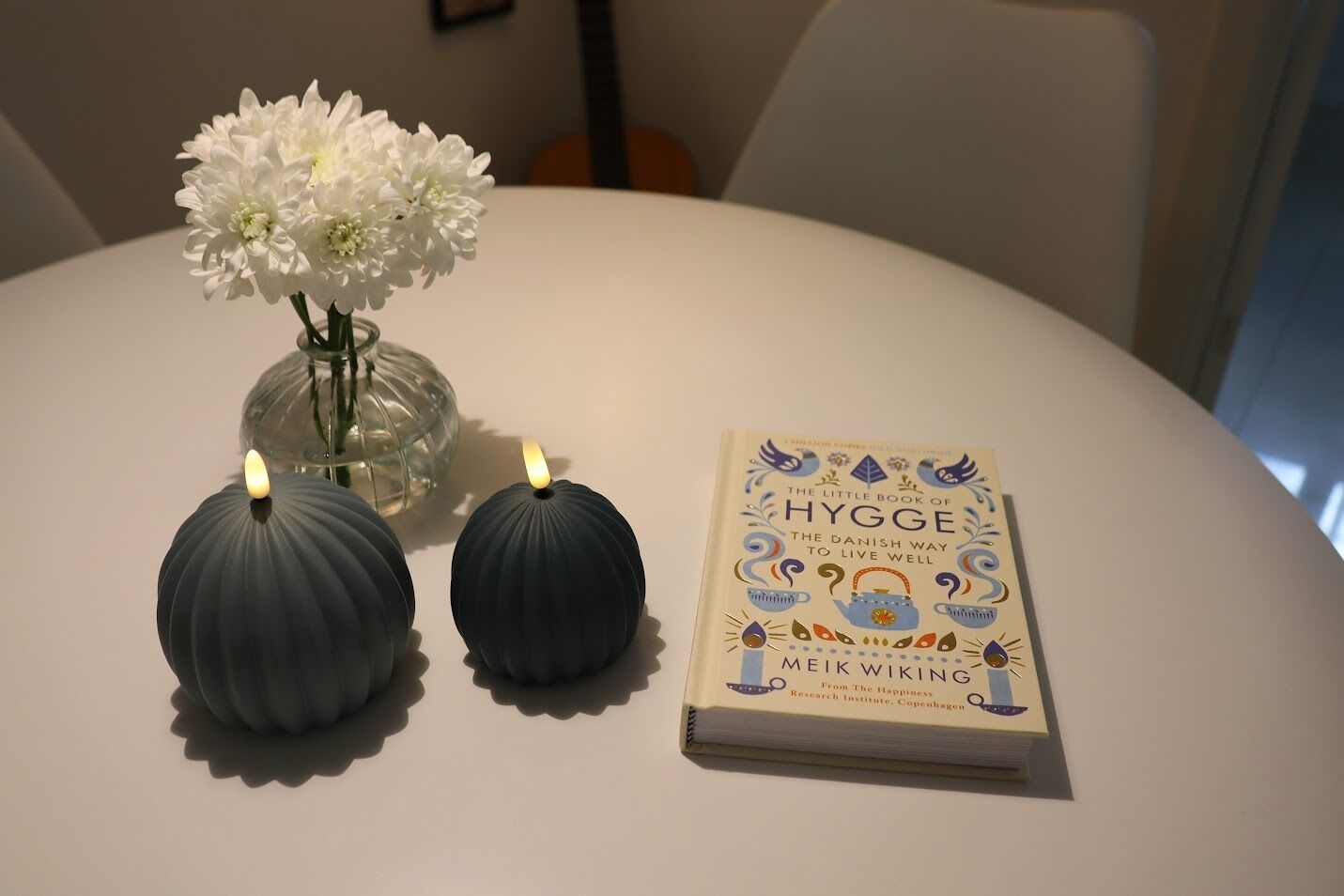 Uma mesa com um livro intitulado 'The Little Book of Hygge' e dois vasos decorativos.