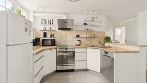 A modern kitchen with white cabinetry, stainless steel appliances, and a wooden countertop. - Møllehuset (Ikast)