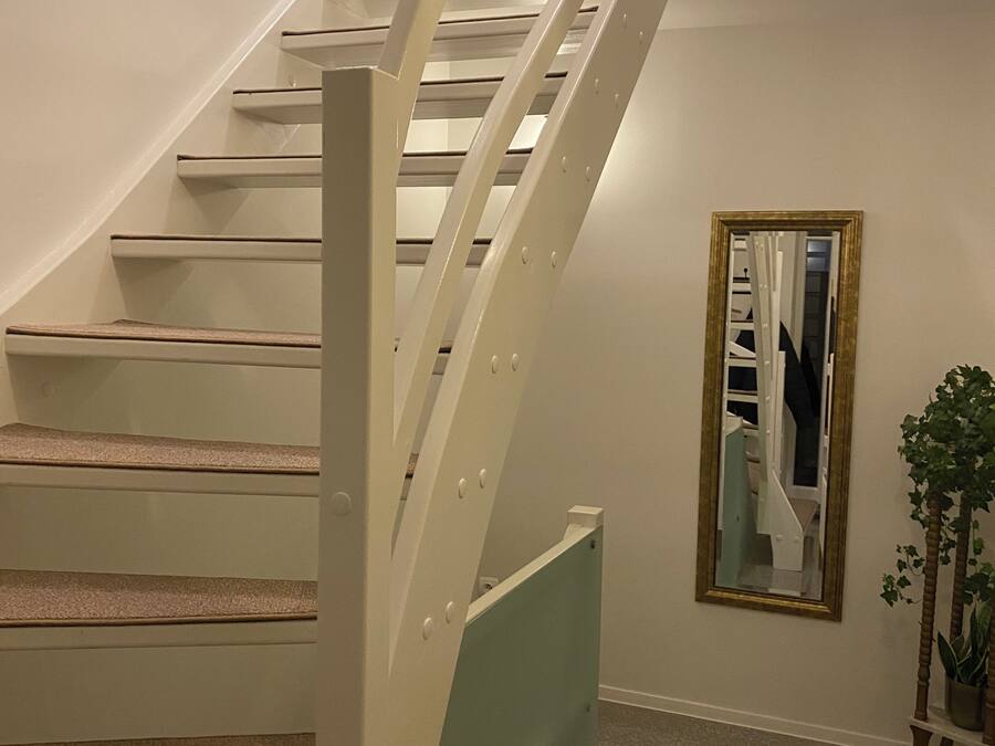 A staircase with white railings and a green handrail, a chandelier, a mirror, and a potted plant.