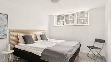 Une chambre à coucher avec un lit, une fenêtre avec des stores, une chaise et une petite table.