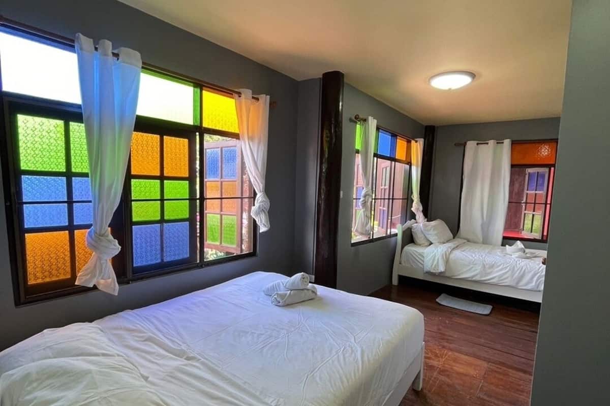 Habitació d'hotel amb un llit gran, un altre més petit i una zona de seients. Hi ha finestres amb vidres de colors i cortines.