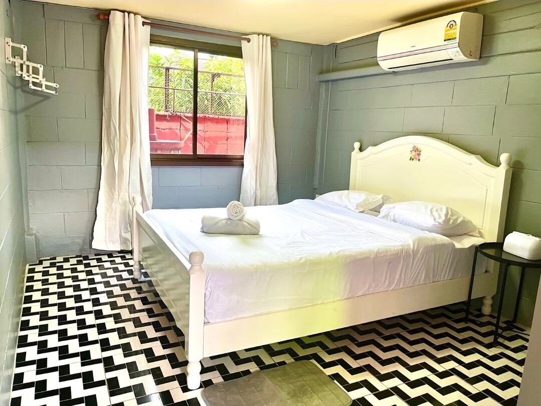 A room with a bed, a window with curtains, a wall-mounted air conditioner, and a patterned floor.