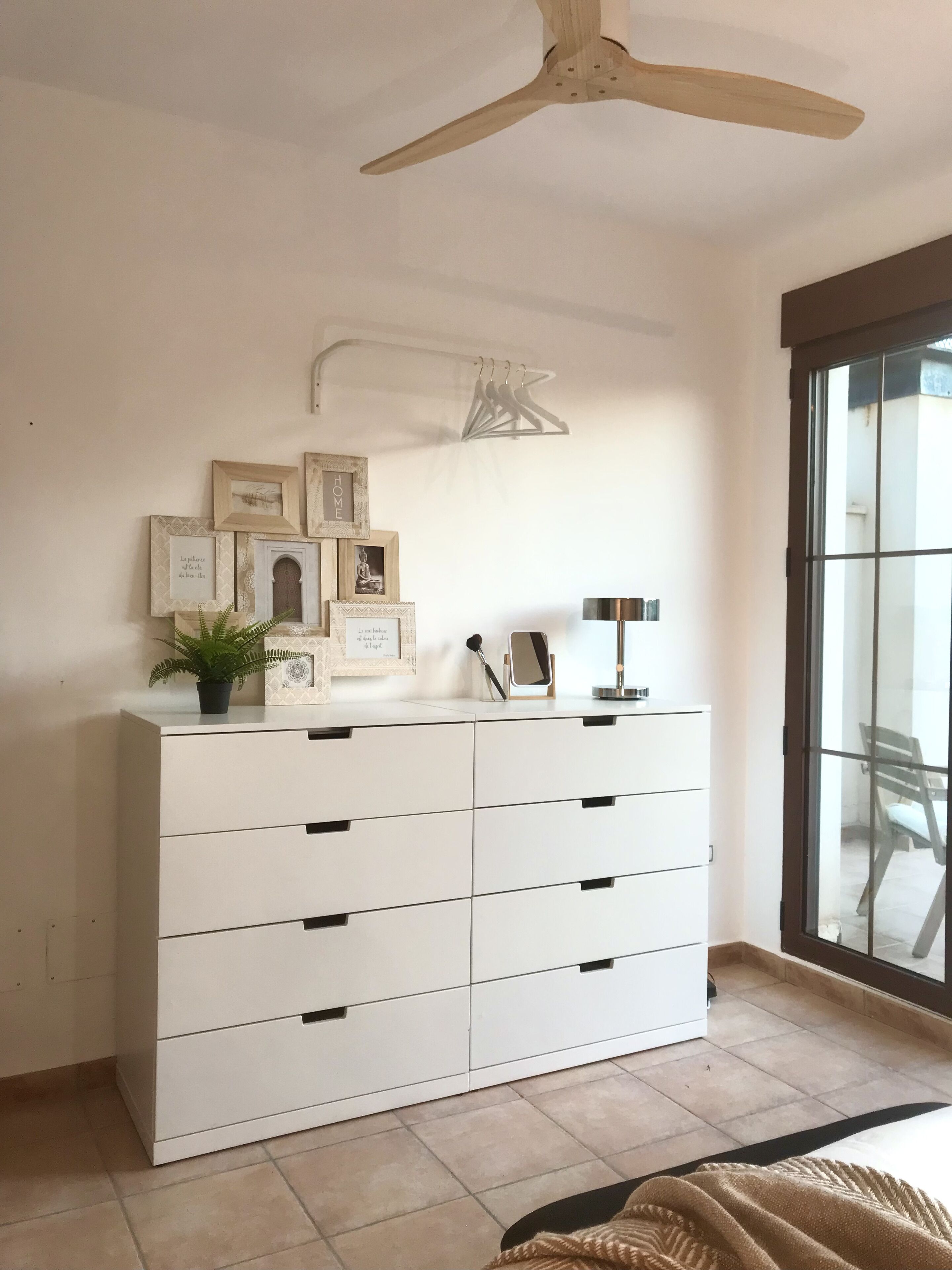 A room with a white chest of drawers, a ceiling fan, and a window with a view of the outside.