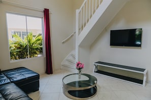 A living room with a glass coffee table, a sofa, a TV, and a staircase. - Cozy 1-bedroom-apartment 2 km From Eagle Beach (Noord)