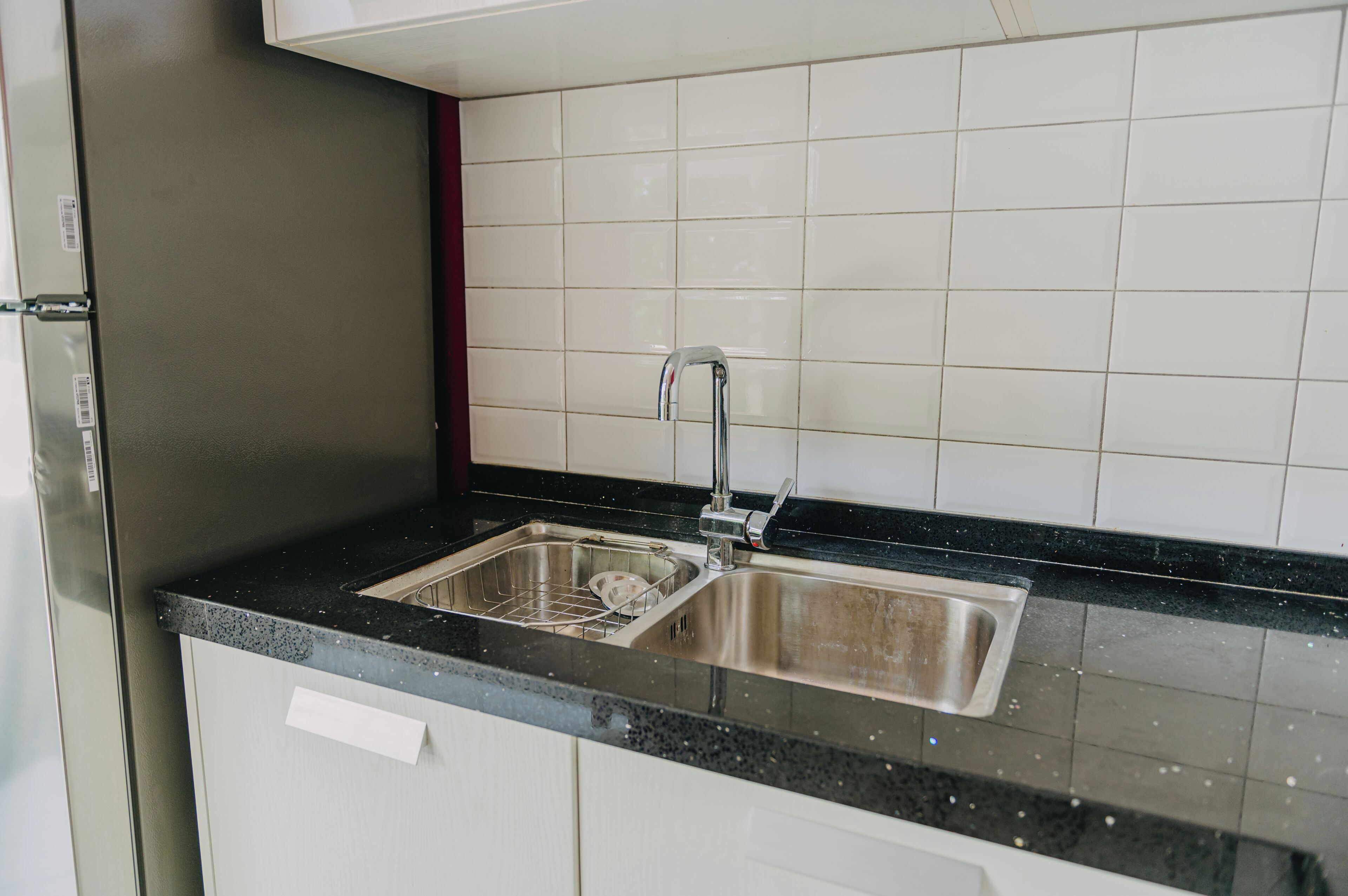 A kitchen with a stainless steel sink, a dish rack, and a refrigerator.