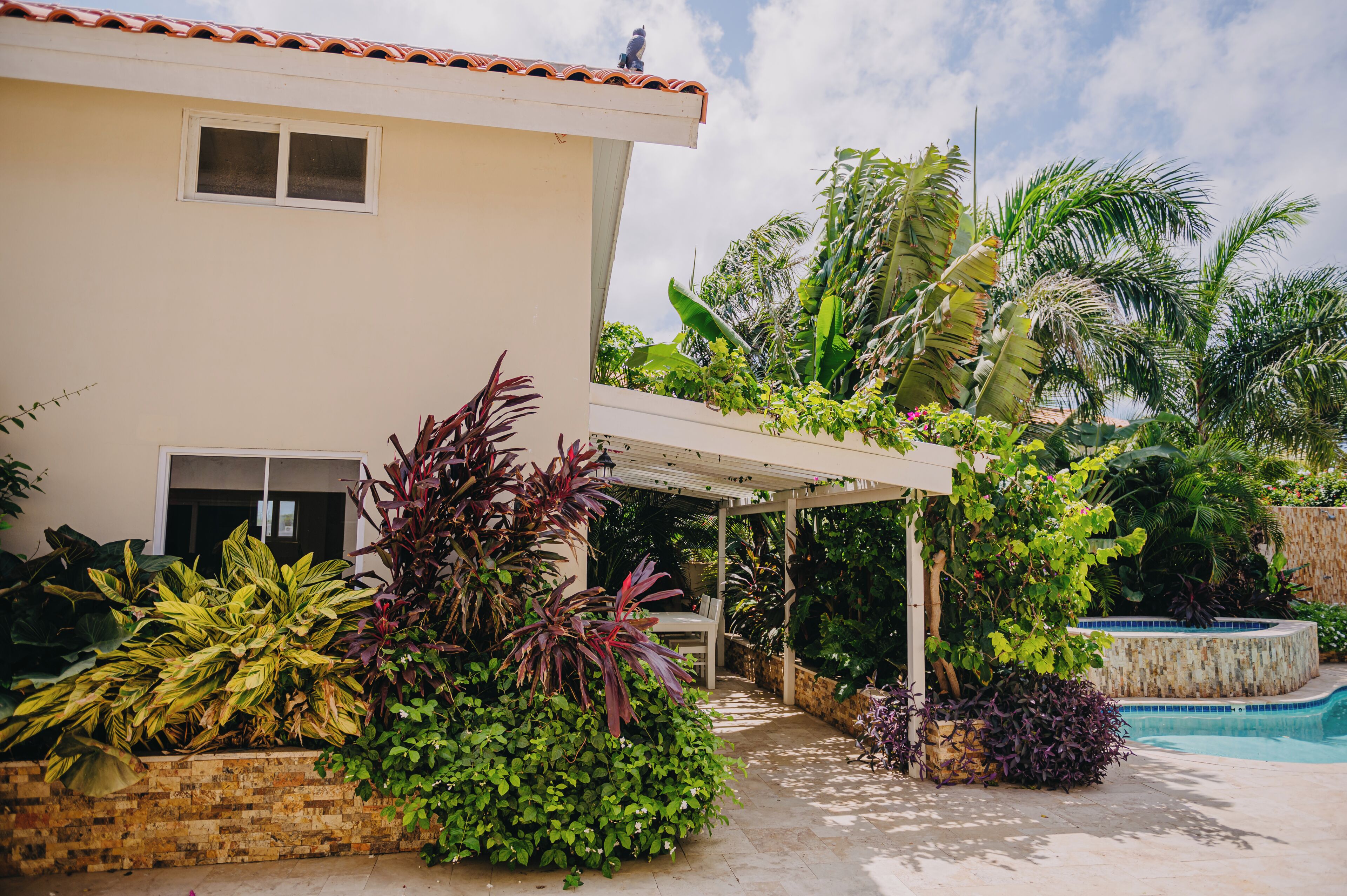 A house with a covered patio, a swimming pool, and lush tropical plants.