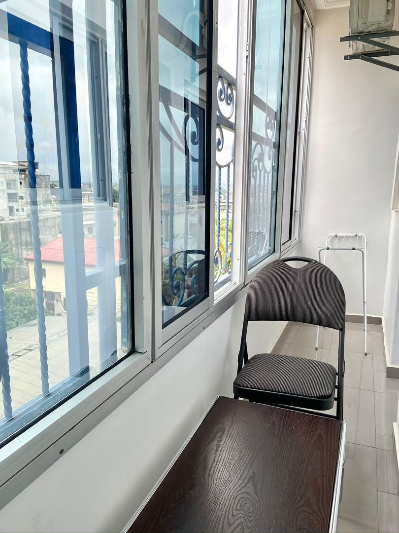 Un balcón con vistas a edificios, una silla de metal y un atril de metal blanco.