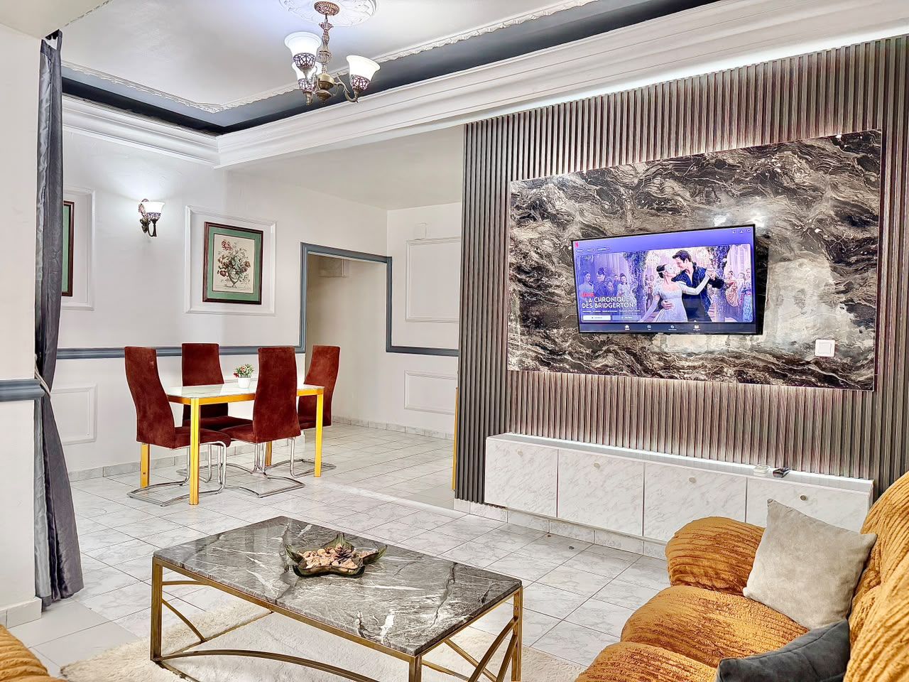 Una sala de estar moderna con una televisión, un comedor con sillas rojas y una mesa de centro de mármol.