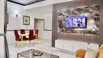 Una sala de estar moderna con una televisión, un comedor con sillas rojas y una mesa de centro de mármol.