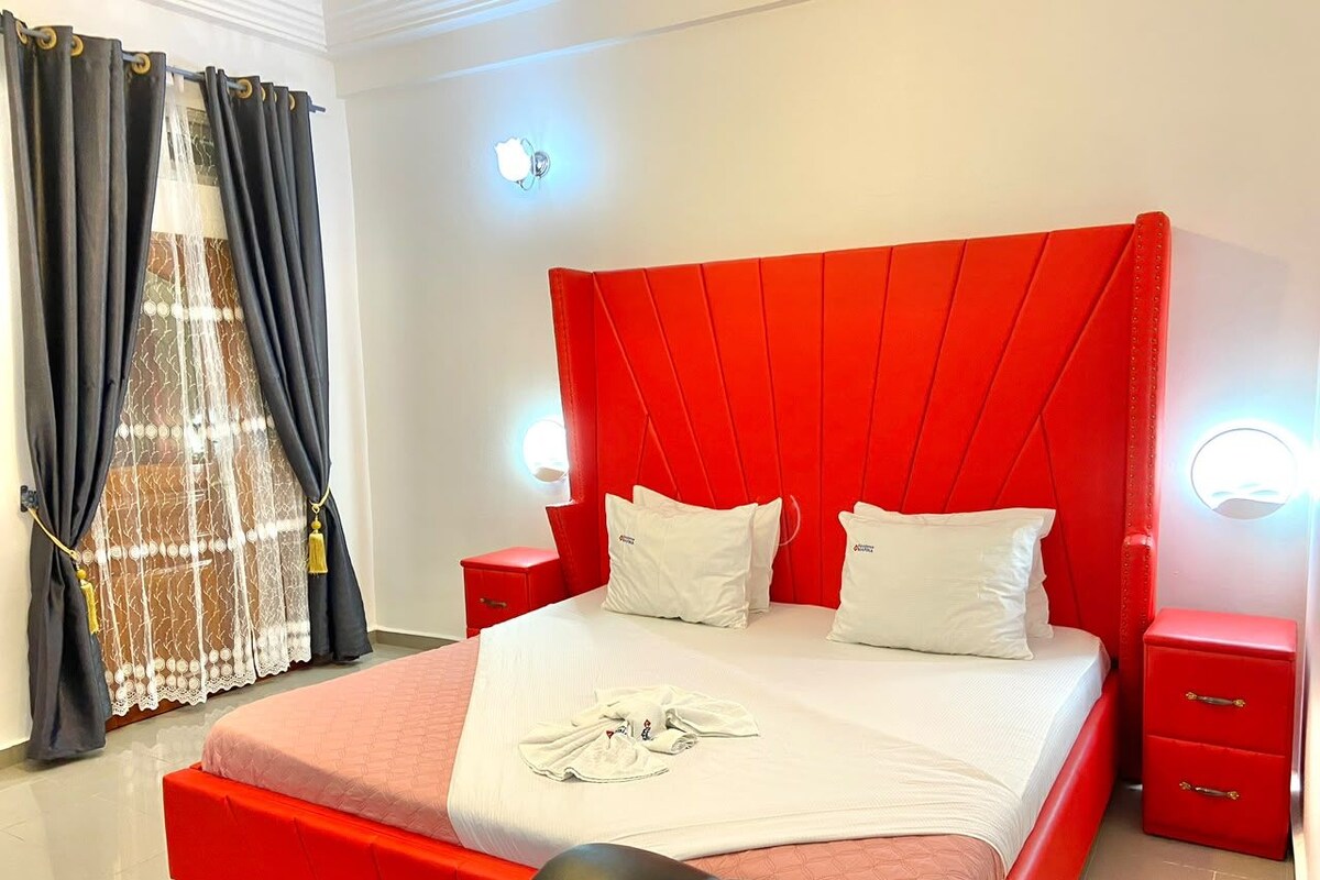 Een hotelkamer met een rood bed, witte kussens, een rode nachtkastje en een rode bijzettafel.