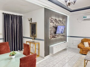 A modern living room with a television, a sofa, a dining table with chairs, and a decorative plant. - Residence La Marina (Douala)