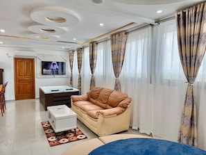 A living room with a sofa, a coffee table, a TV, and curtains. - Residence La Marina (Douala)