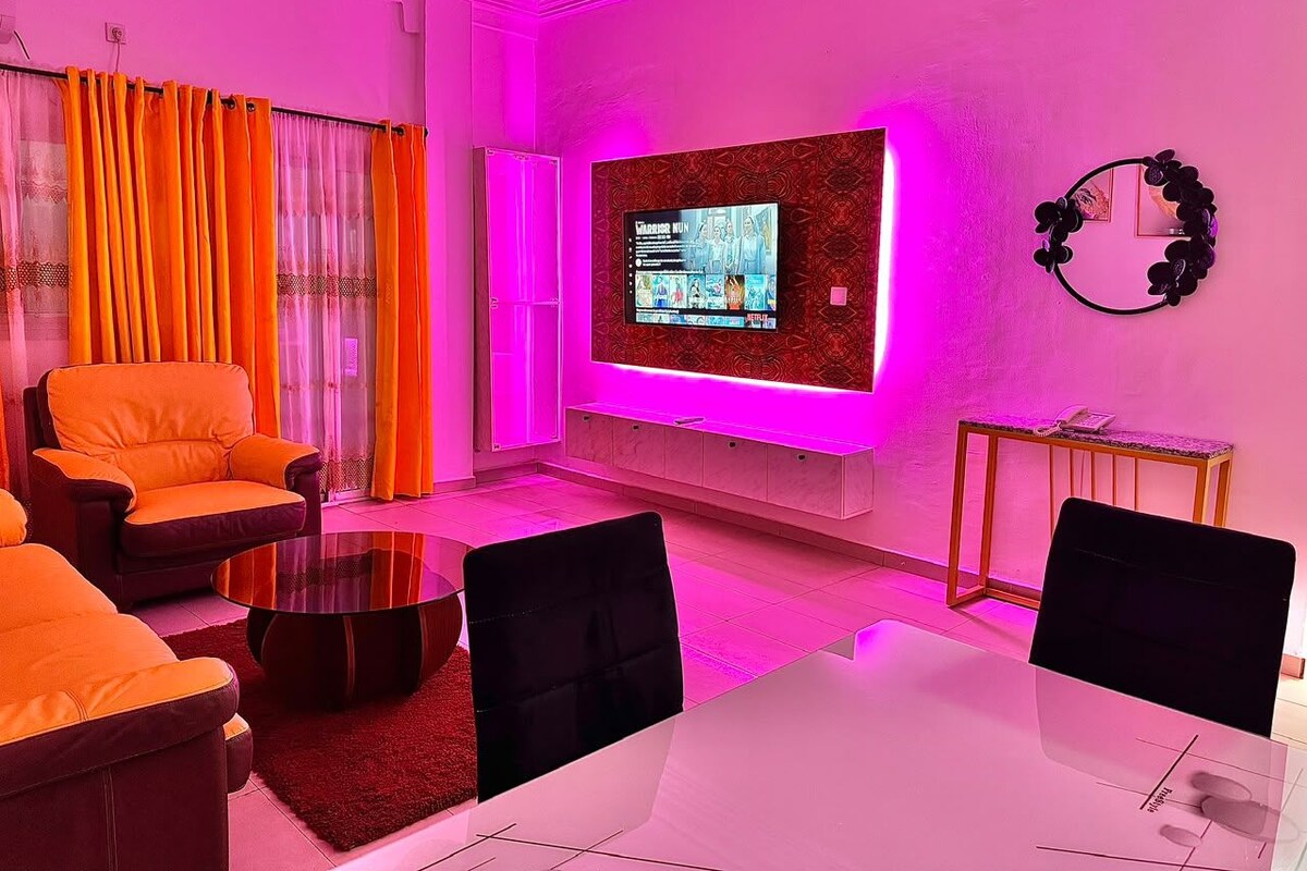 Een moderne woonkamer met een flatscreen televisie, oranje meubels en een roze gloed.