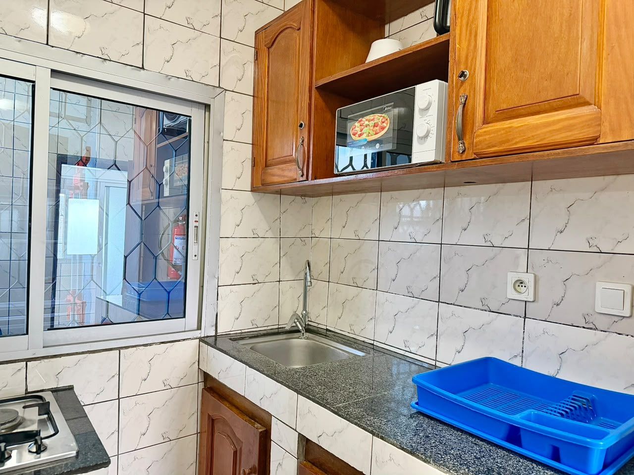 Una cocina con ventana, un lavamanos, armarios y un contenedor azul.