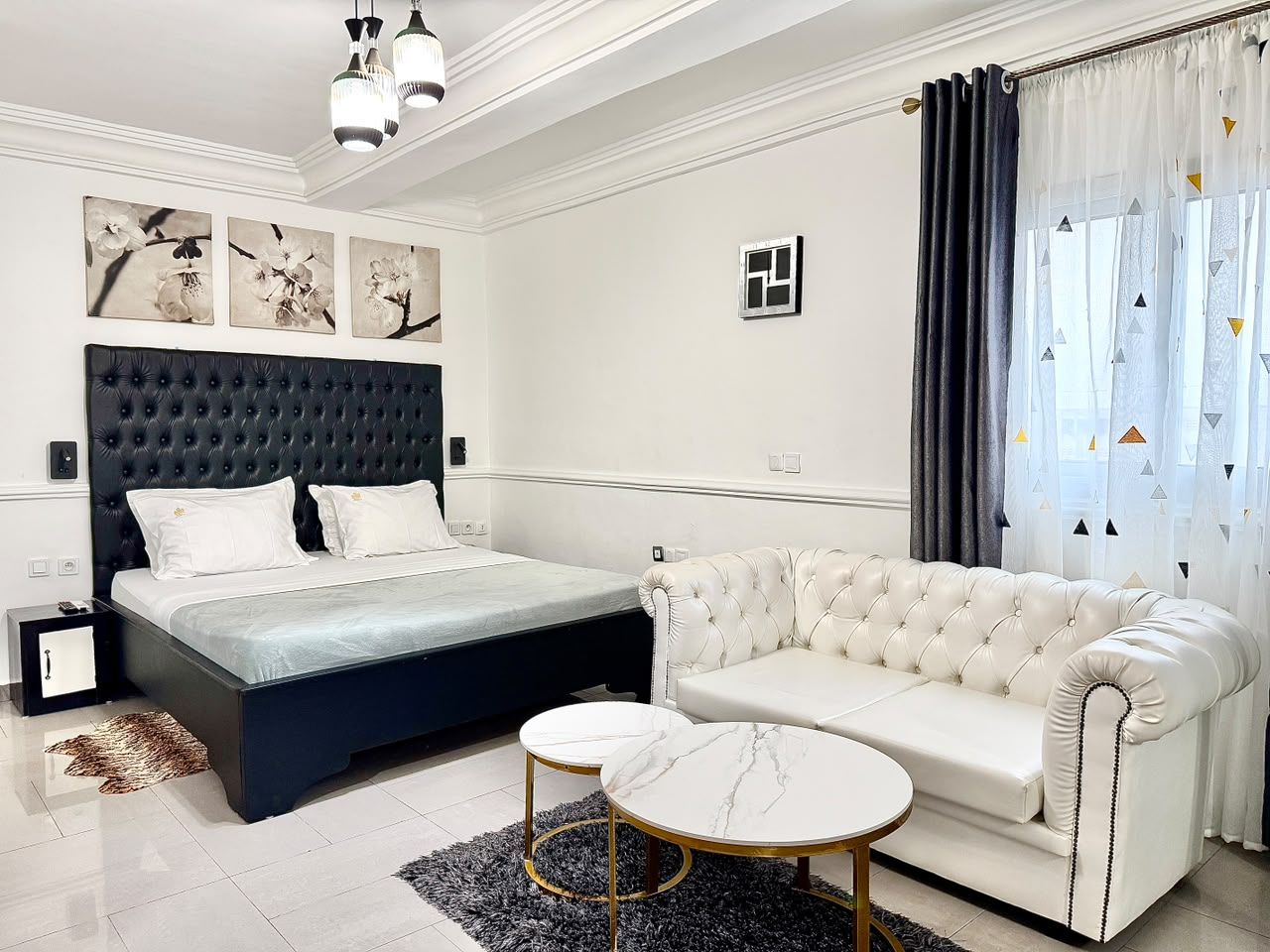 A bedroom with a bed, a white sofa, two round tables, and artwork on the wall.