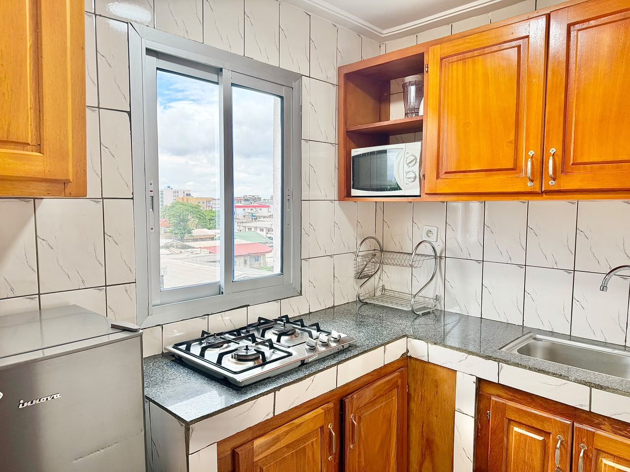 A kitchen with a gas stove, wooden cabinets, a microwave, and a window with a view of buildings.