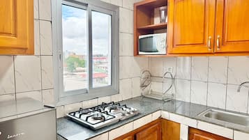 A kitchen with a gas stove, wooden cabinets, a microwave, and a window with a view of buildings.