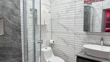 Un baño moderno con cabina de ducha de vidrio, inodoro blanco y tocador con lavamanos.