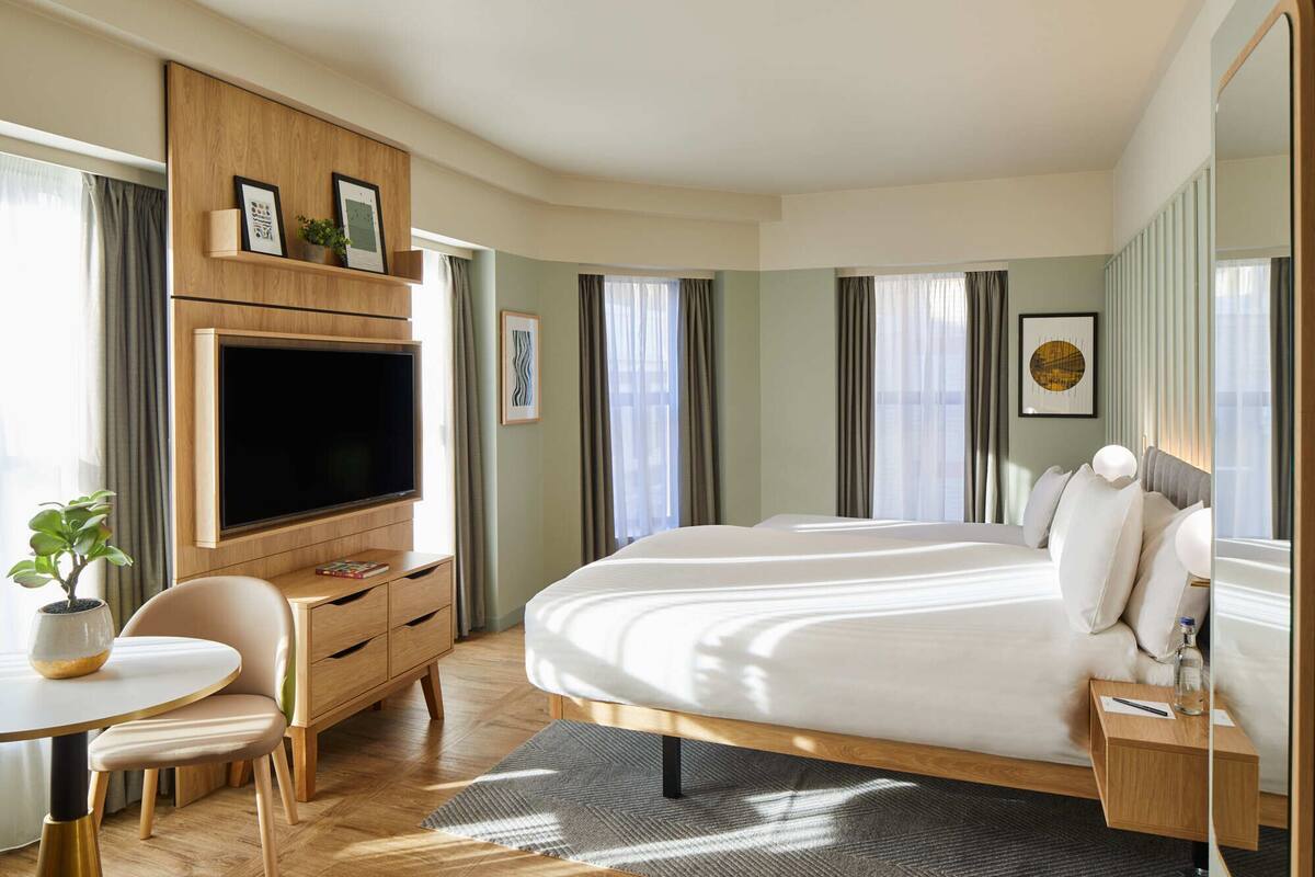 Une chambre d’hôtel moderne dotée d’un grand lit, d’un téléviseur à écran plat, d’un bureau en bois et d’une petite table agrémentée d’une plante.