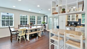 Una cocina amplia con comedor, piso de madera y armarios blancos.