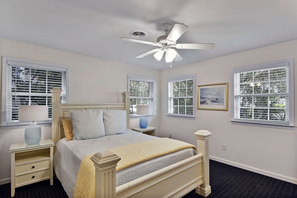 A bedroom with a bed, nightstands, a ceiling fan, and windows with blinds.