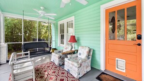 A porch with a white bench, two armchairs, a red lamp, and a ceiling fan. - 450 ft to East Beach • 2 Kings • Pet Friendly • Sleeps 6 • St. Simons Island (Saint Simons Island)