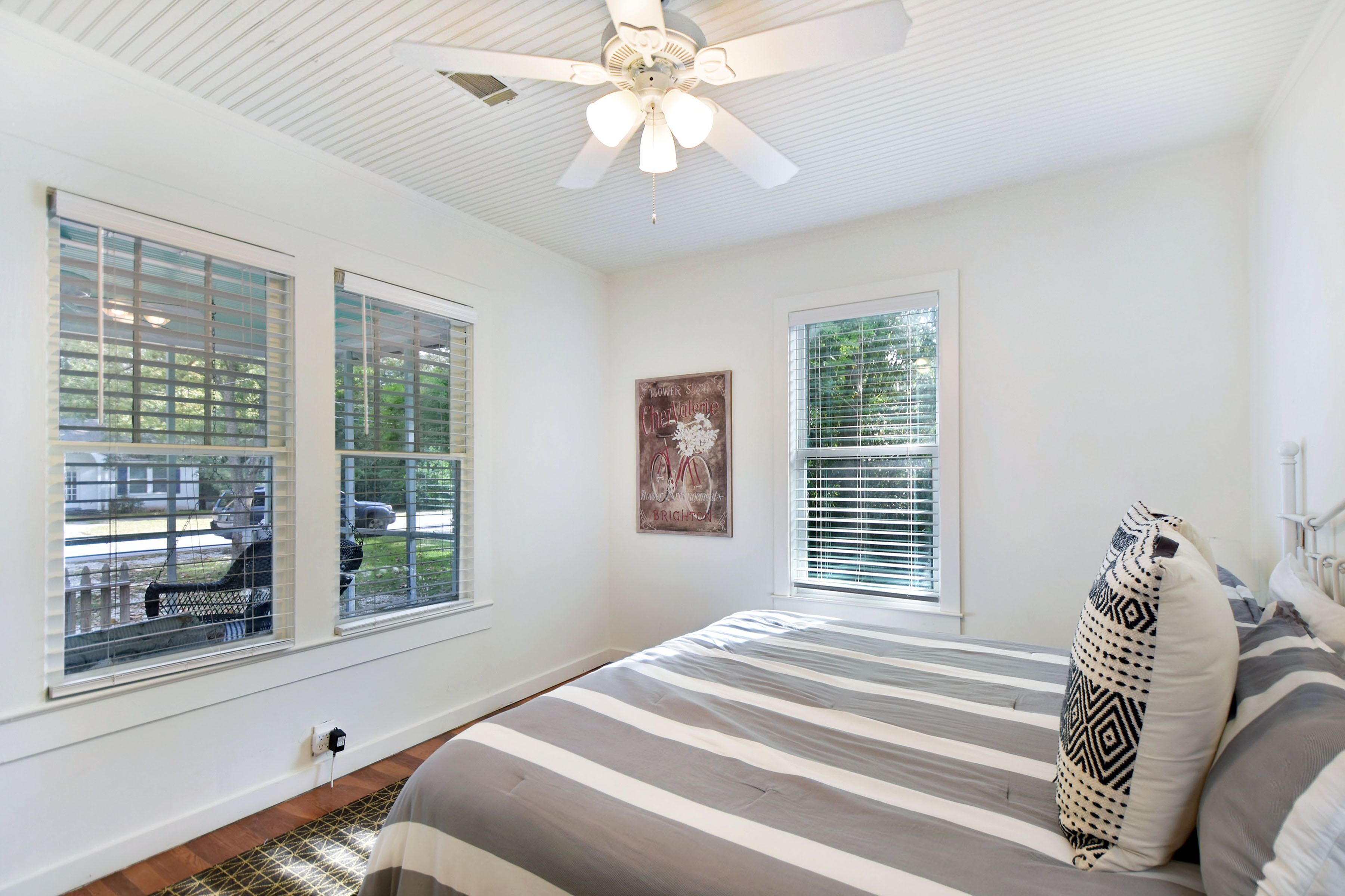 A bedroom with a bed, a ceiling fan, and two windows with blinds.