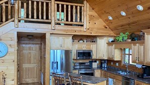 A spacious kitchen with wooden cabinets, a central island with bar stools, a dining table, and a staircase leading to an upper level. - Mountain Home with Views for Miles!!! (Murphy)