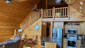 A spacious cabin interior with a wooden interior, a kitchen with modern appliances, a dining area with chairs, and a staircase leading to a loft. - Mountain Home with Views for Miles!!! (Murphy)