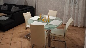 A dining area with a glass table, four chairs, a black sofa, a floor lamp, and a curtain with a pattern. - Gemütliche Ferienwohnung im Grünen, in der Nähe von Lüneburg (Melbeck)