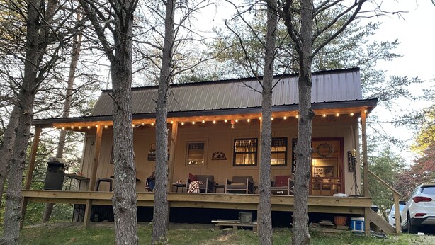 A rustic cabin with a porch, wooden deck, and string lights.