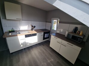 A compact kitchen with white cabinets, a dishwasher, a microwave, and a window providing natural light.