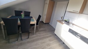 A compact kitchen with a dining area, a built-in oven, and a white door with a brass handle. - Monteurzimmer Gelnhausen, Ferienwohnung, Auch für Große Gruppen, Nähe Frankfurt (Gelnhausen)
